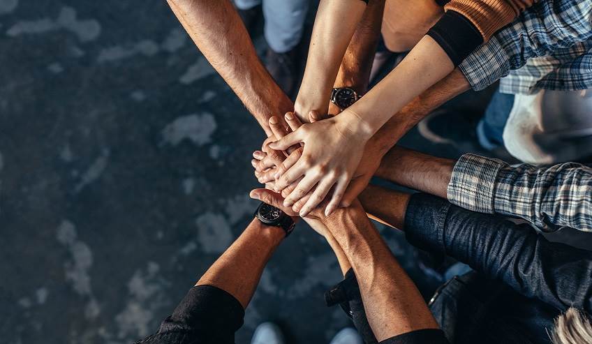 Top view of creative professionals putting their hands together as a symbol of teamwork, cooperation and unity. Stack of hands of men and woman.